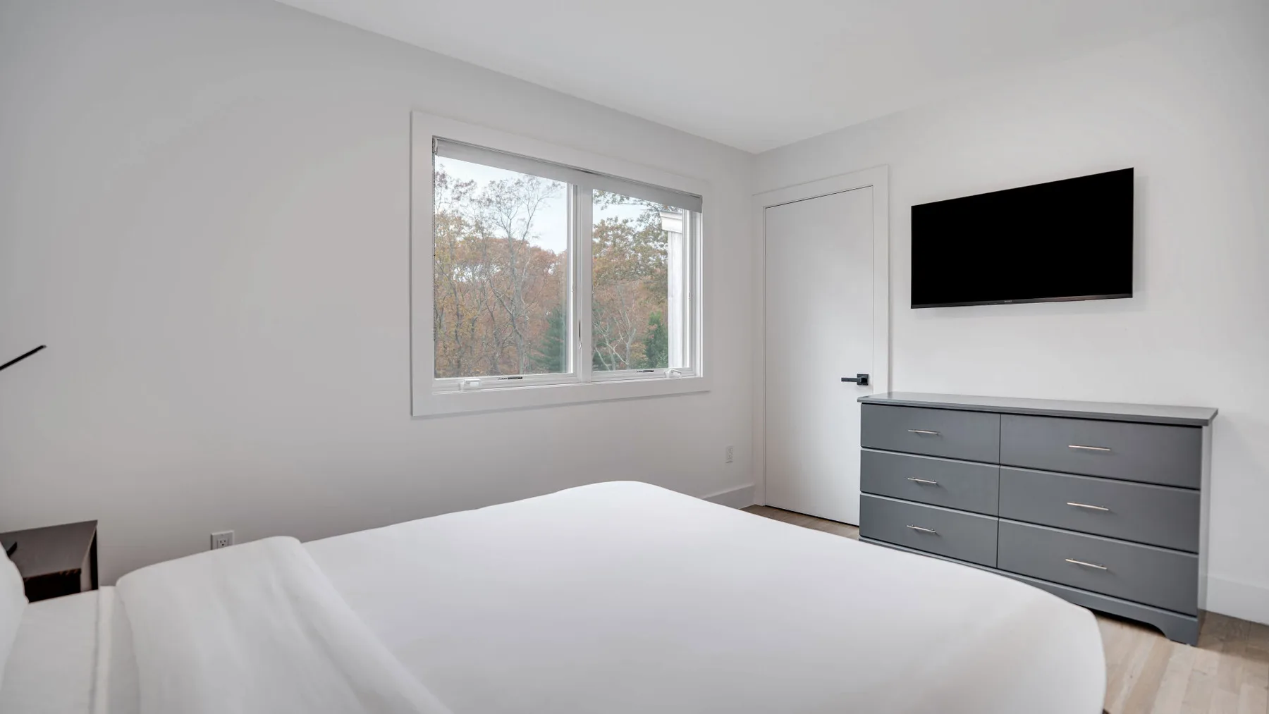 Un dormitorio luminoso con una cama grande, una ventana y un televisor sobre una cómoda.