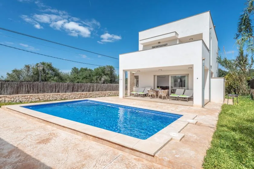 Una casa blanca moderna se encuentra junto a una piscina rectangular y asientos al aire libre.