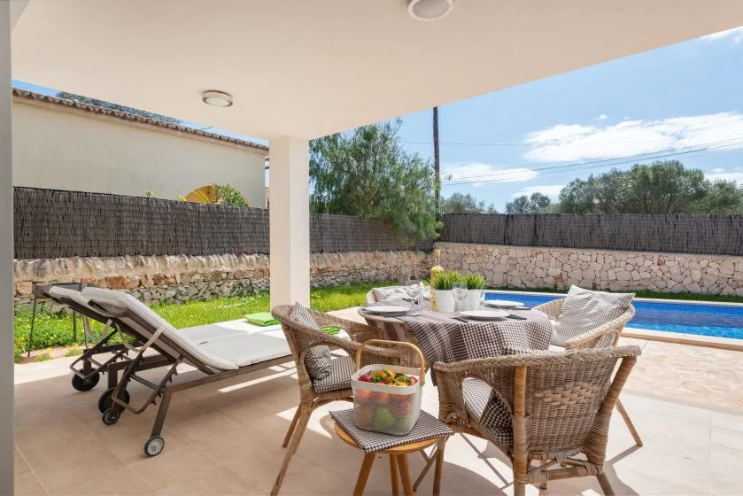 Un patio cubierto con asientos al aire libre y una piscina al fondo.