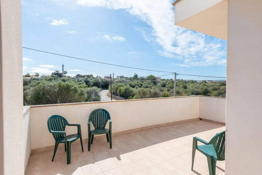 Una terraza embaldosada con asientos verdes da a un amplio paisaje de arbustos.