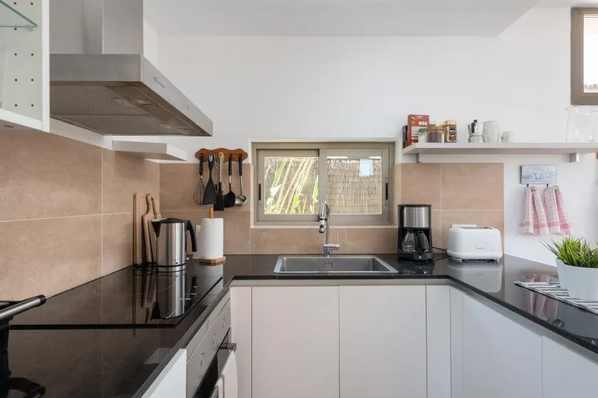 Una cocina luminosa con encimeras oscuras, armarios blancos y una ventana sobre el fregadero.