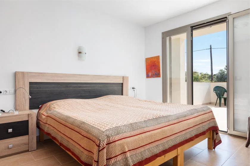 Un dormitorio con una cama doble junto a una puerta de vidrio abierta.