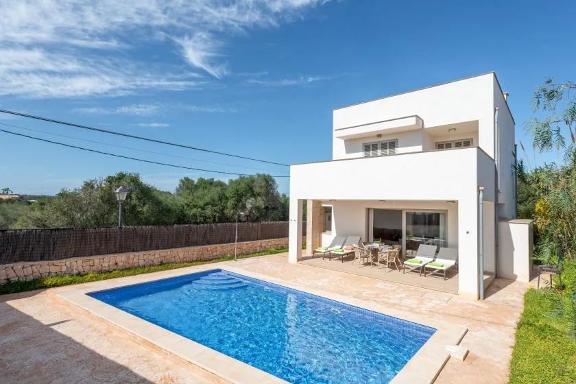 Una casa moderna da a una piscina rectangular y un patio con asientos al aire libre.