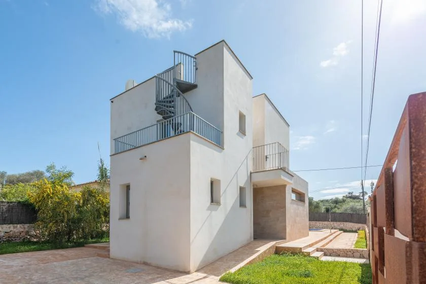 Una casa blanca moderna con escaleras metálicas exteriores se alza junto a un patio pavimentado.