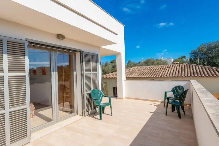 Una terraza exterior soleada junto a un edificio, con puertas corredizas de vidrio y asientos.