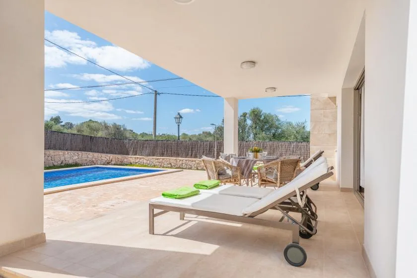 Un patio cubierto con tumbonas da a una piscina y una zona de estar al aire libre.