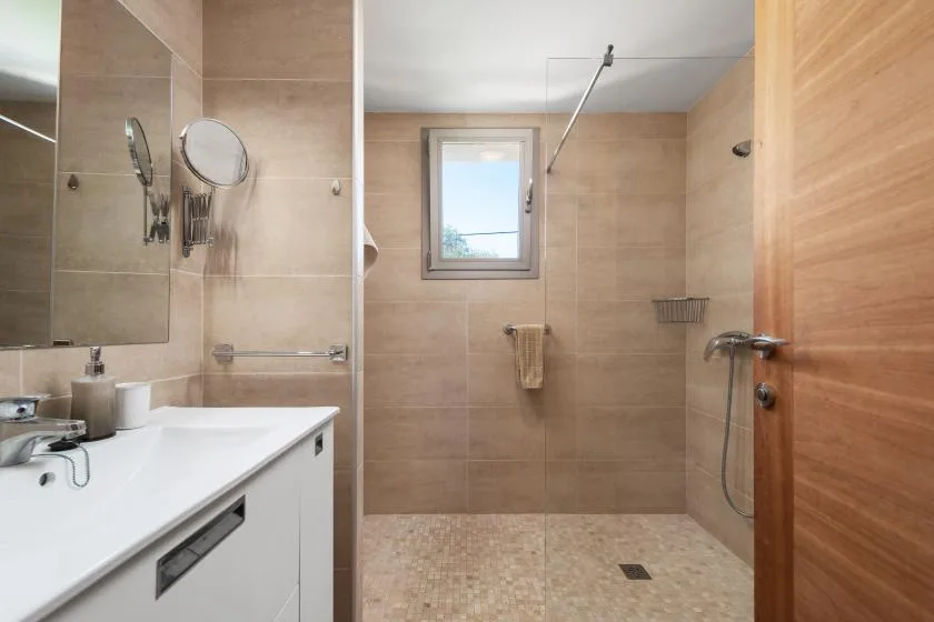 Un baño con ducha a ras de suelo, lavabo y una ventana pequeña.