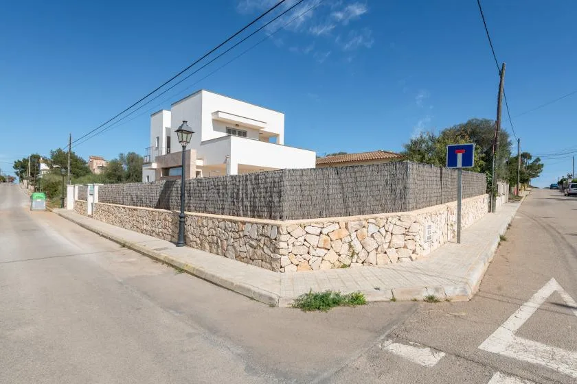 Una casa blanca moderna se alza detrás de un muro de piedra en una esquina.