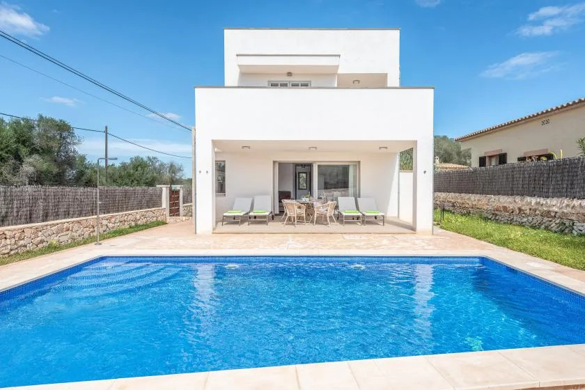 Una piscina está frente a una casa blanca moderna con un patio cubierto.