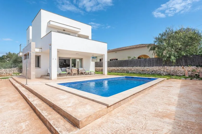 Una casa blanca moderna da a una piscina rectangular y un patio pavimentado.