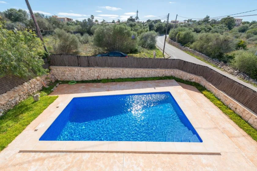 Una piscina ocupa una zona exterior pavimentada, rodeada de muros de piedra y vegetación.