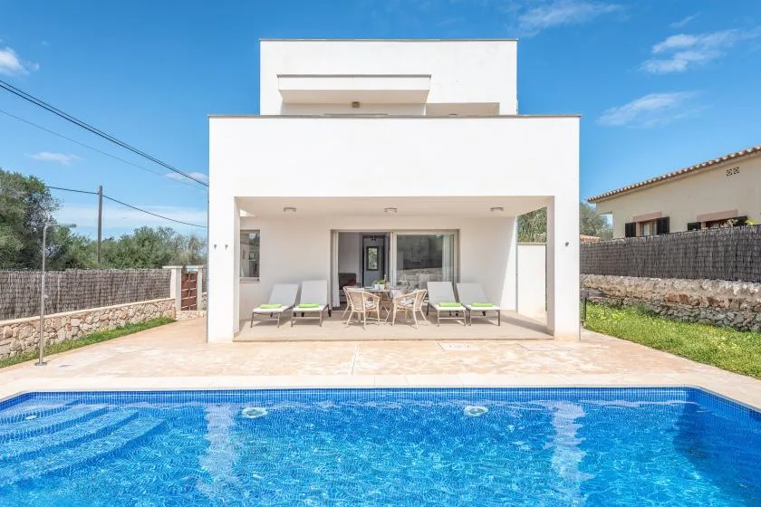 Una casa blanca moderna da a una piscina, con asientos al aire libre en el patio.