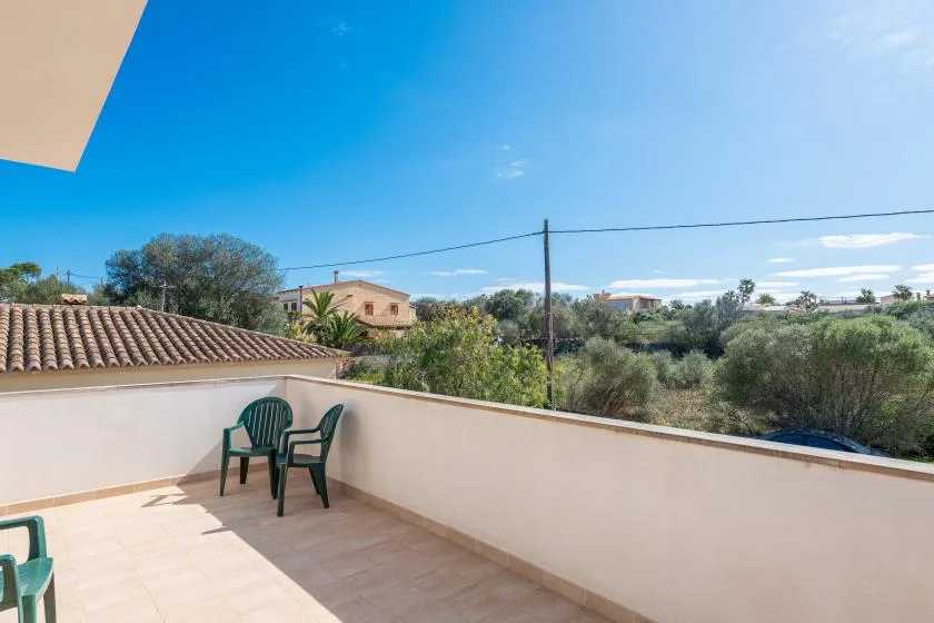 Una terraza exterior soleada tiene suelo de baldosas, muros bajos y asientos con vistas a la vegetación.