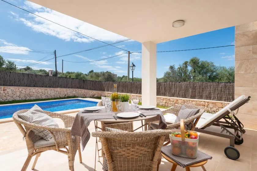 Un patio cubierto con asientos al aire libre da a una piscina y un patio cercado.