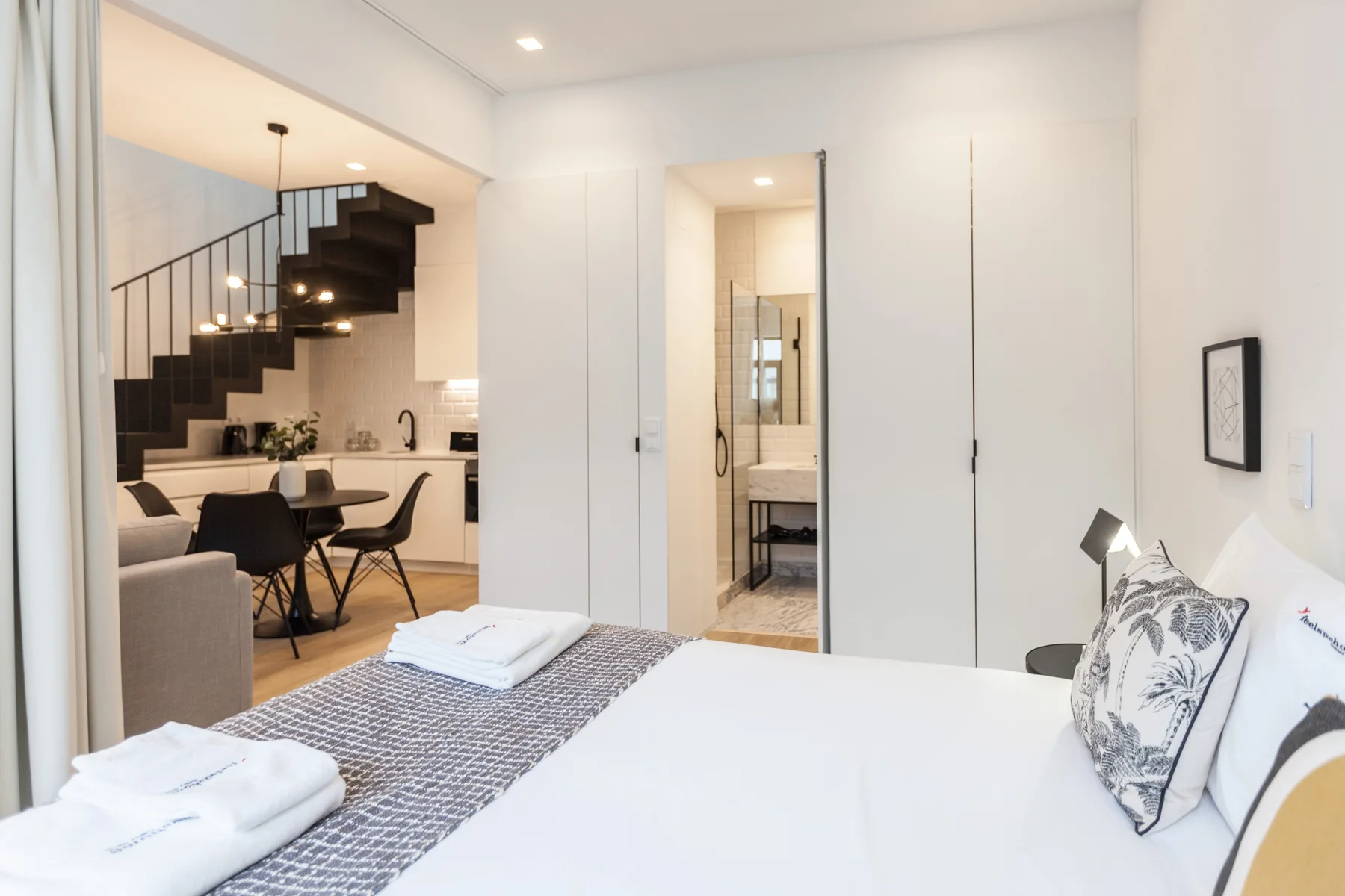 Un dormitorio luminoso con una cama en primer plano y una puerta abierta al baño.