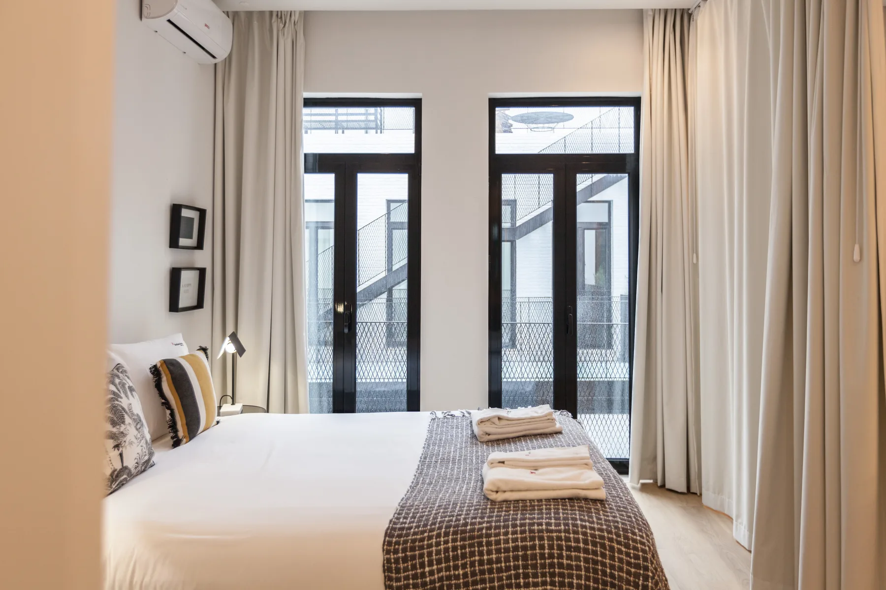 Un dormitorio luminoso con una cama bien hecha y ventanas altas.