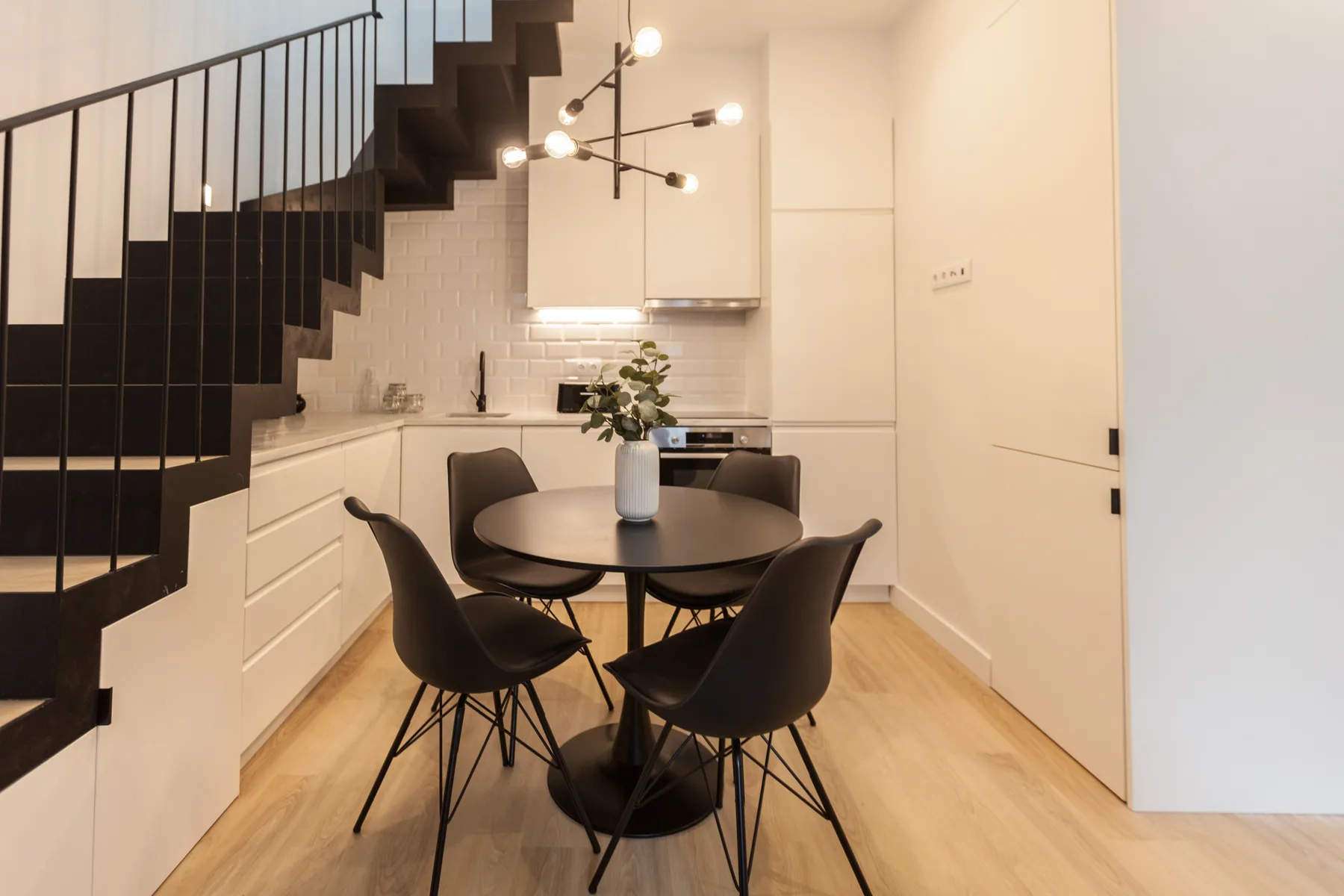 A dining area with a round table and dark seating beneath a staircase.