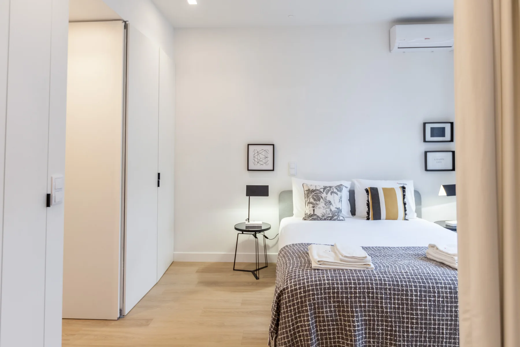 A bright bedroom with a bed, bedside tables, and framed wall art.
