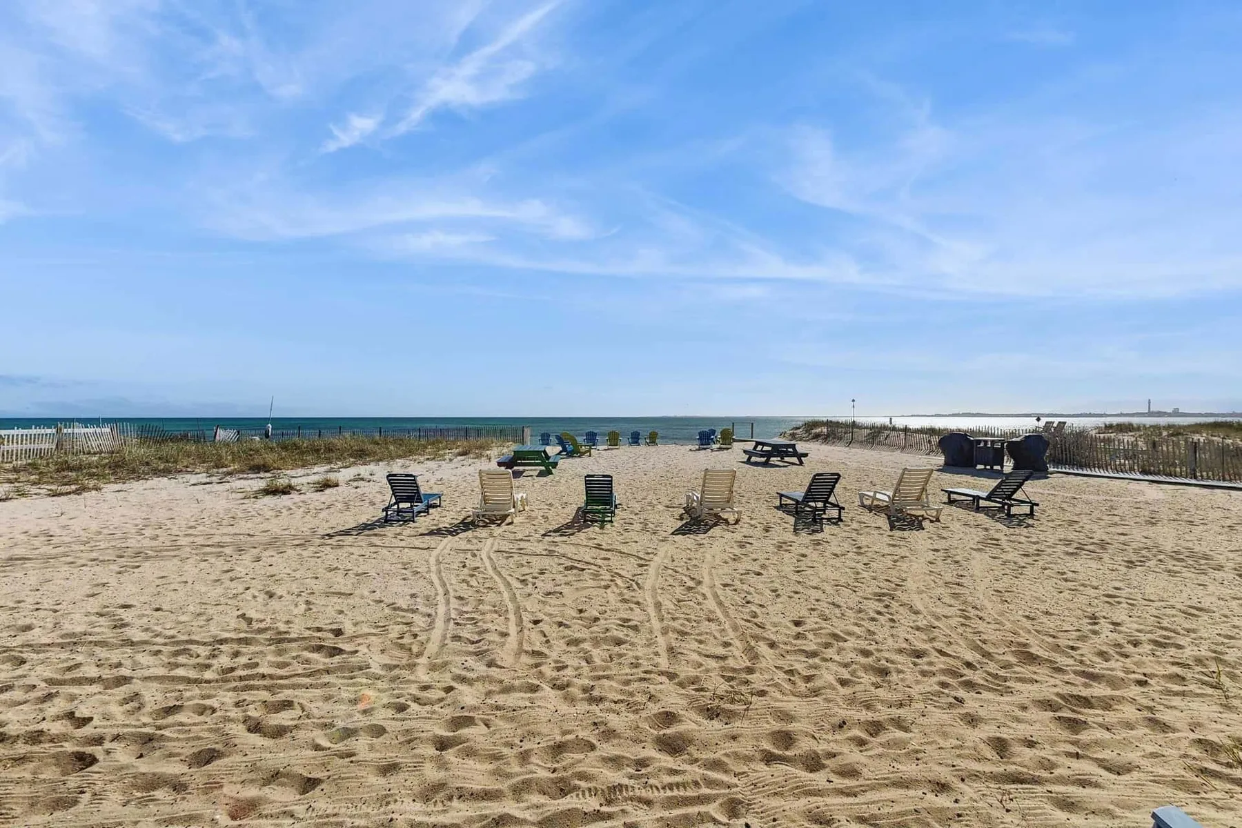 A sandy beach area has scattered seating and a view of the sea.