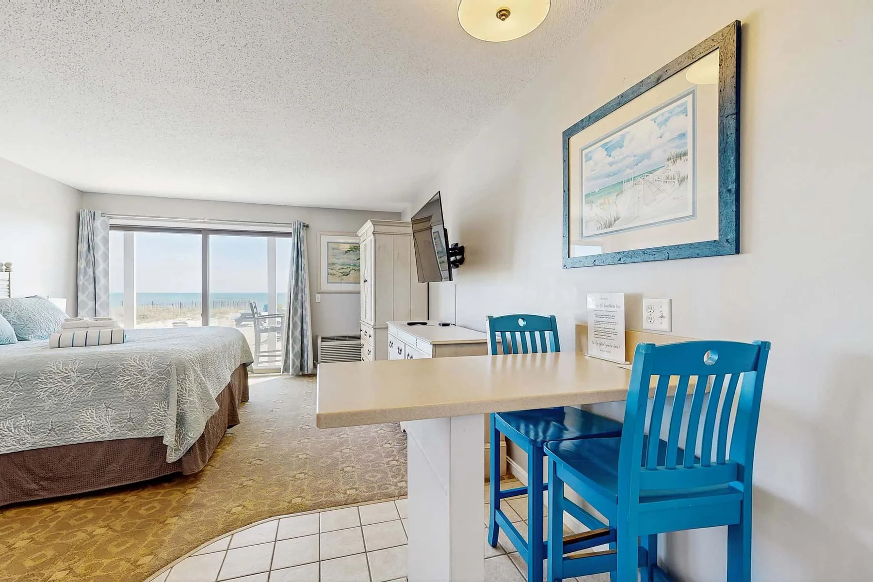 Un dormitorio con una mesa y sillas azules junto a una ventana grande.
