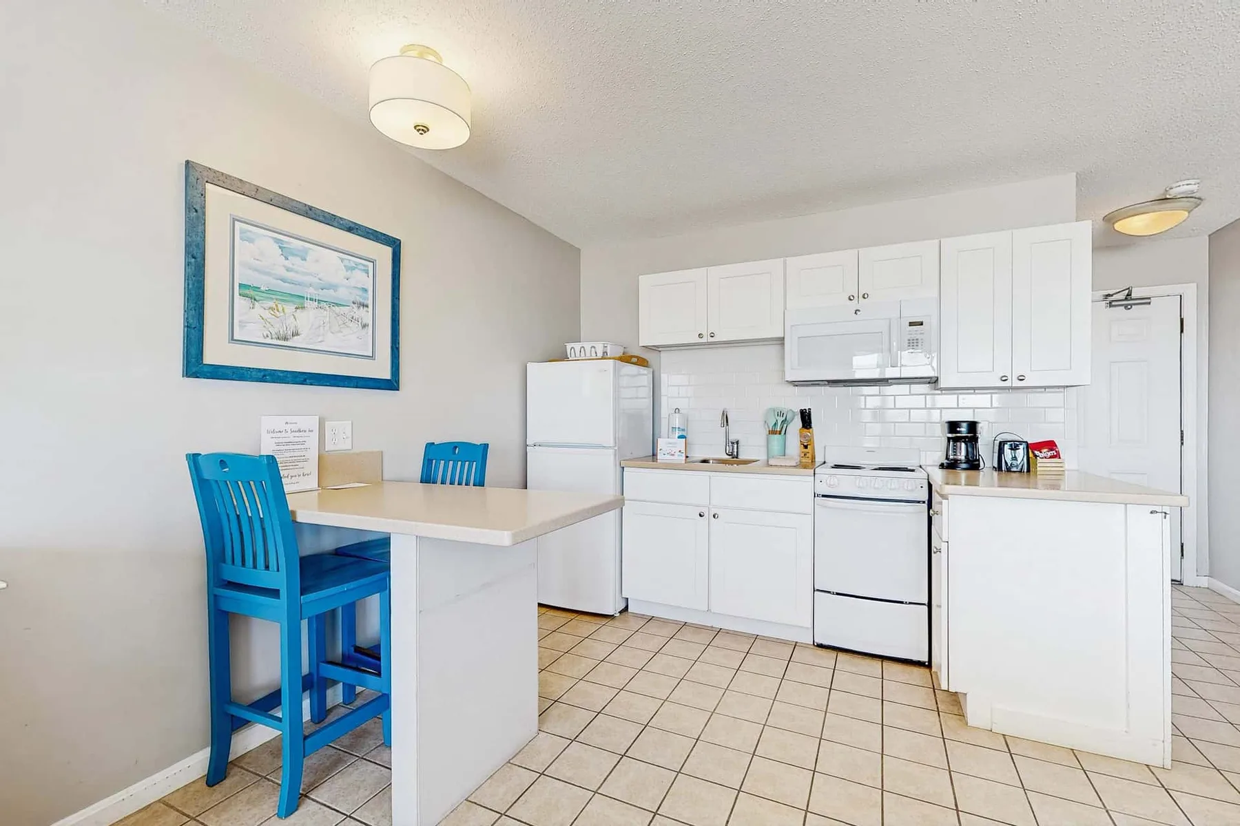 Una cocina luminosa con comedor, asientos azules y gabinetes blancos.