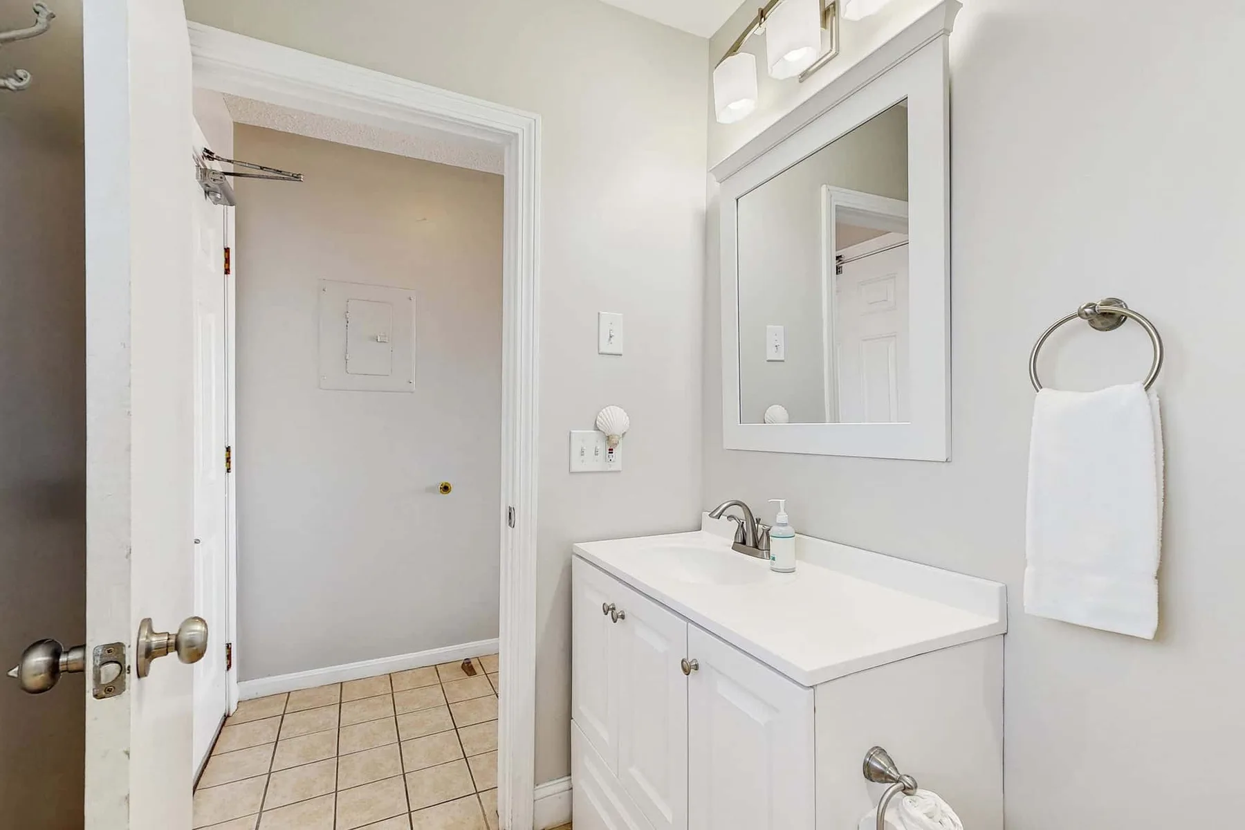 Un lavabo de baño y un espejo están junto a una puerta abierta a un área con suelo de baldosas.