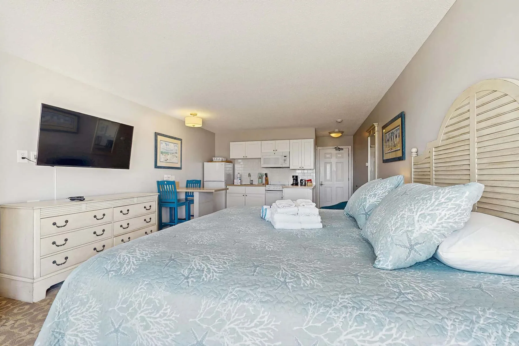 A bedroom with a large bed and a kitchenette in the background.