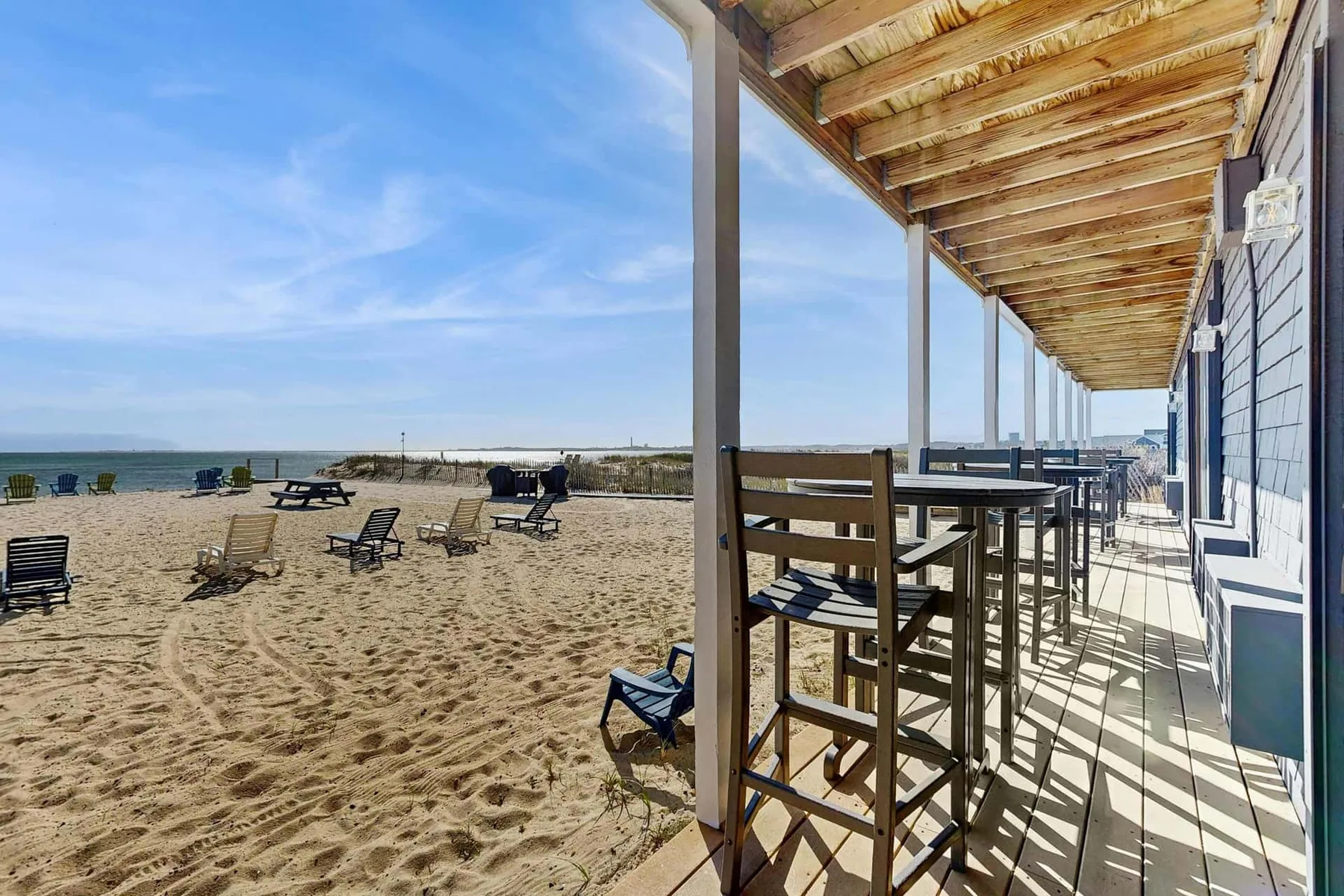 Una terraza junto al mar con asientos altos da a una playa de arena y al océano.