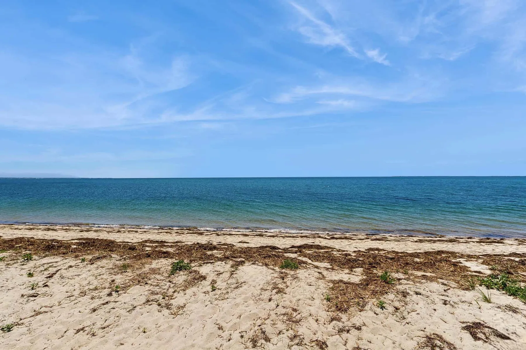Una playa de arena se extiende junto a aguas azules tranquilas bajo un cielo despejado.