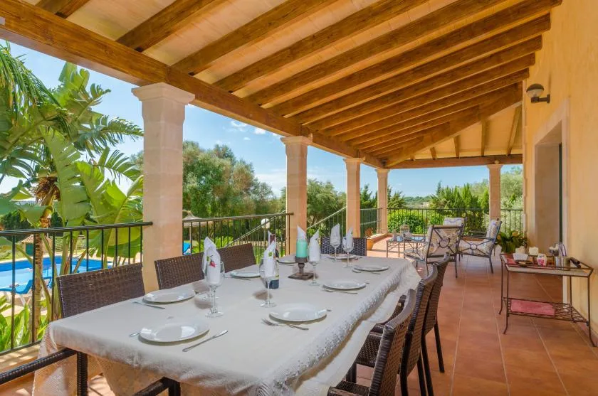Un comedor exterior cubierto con una mesa larga y sillas da a un jardín.