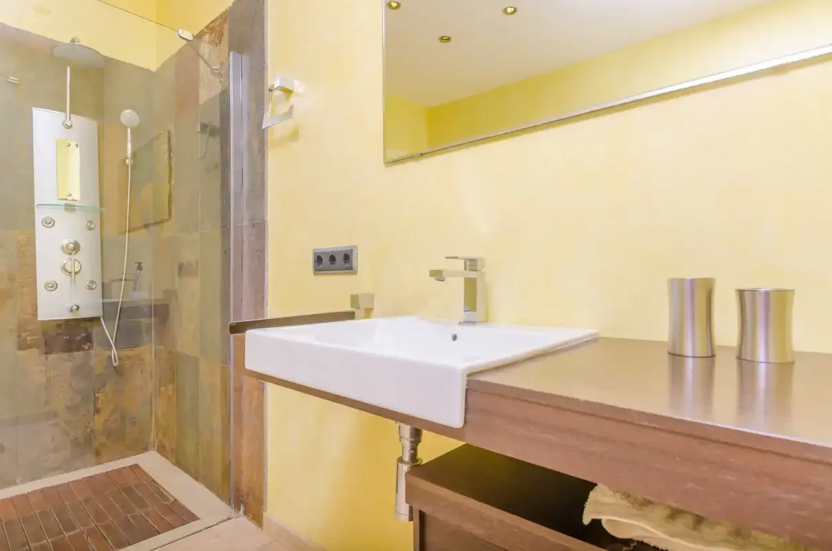 Un baño luminoso con un lavabo blanco junto a una ducha de cristal.