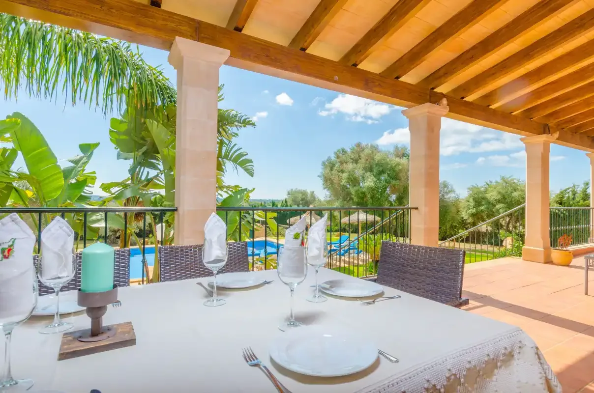 Una zona de comedor exterior cubierta da a un jardín y una piscina.