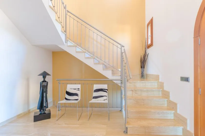 Una escalera luminosa con barandilla metálica y dos asientos debajo.