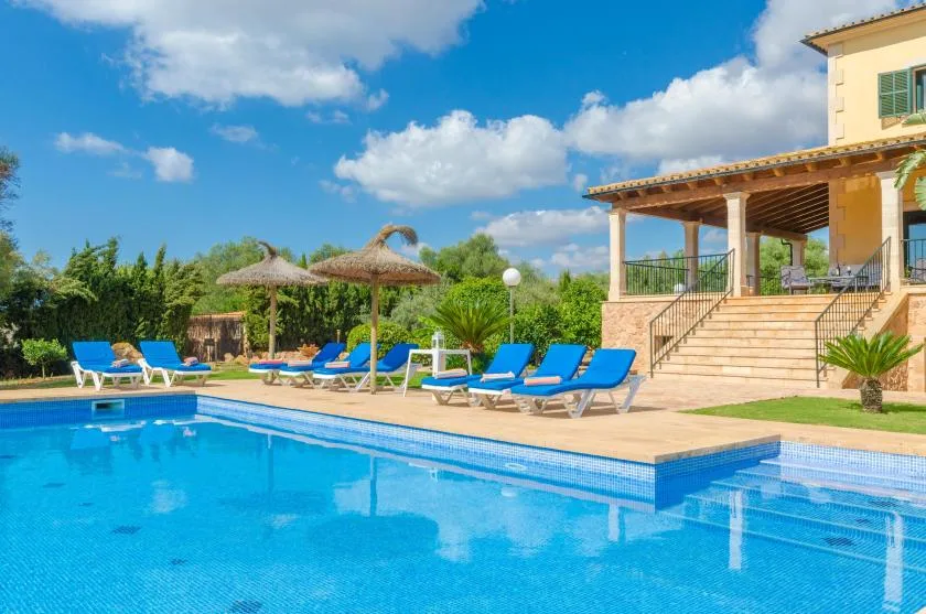 Una piscina al aire libre junto a un patio con asientos y una terraza cubierta.