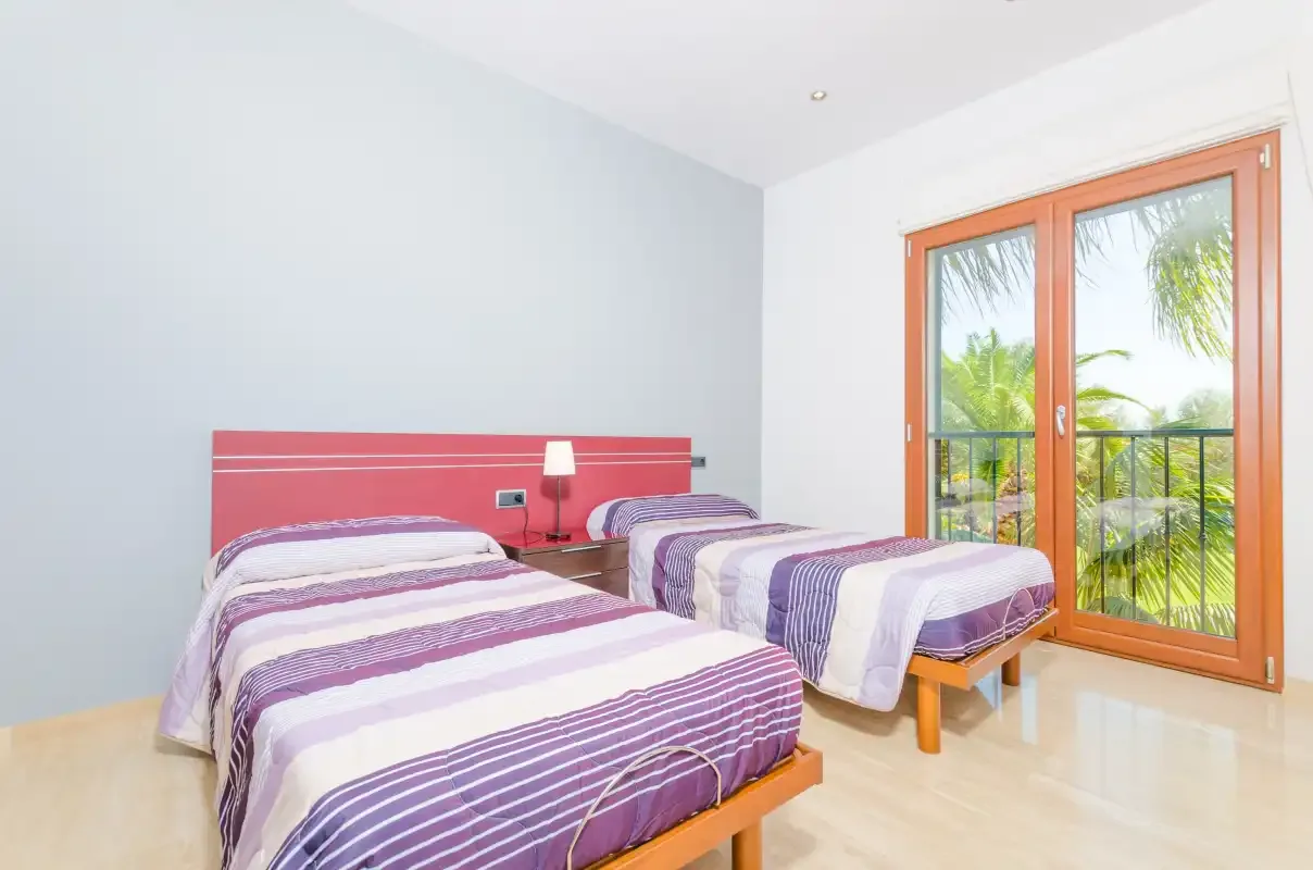 Un dormitorio con dos camas junto a grandes puertas de vidrio que dan a un balcón.