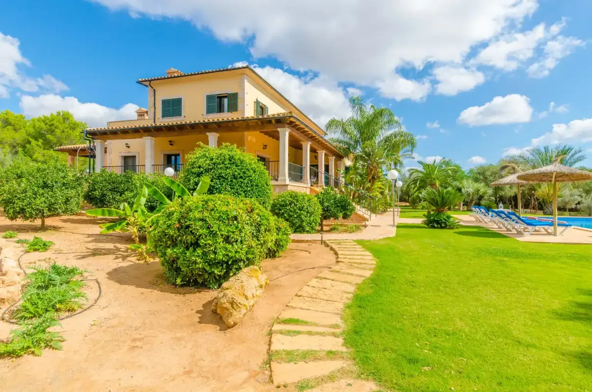 Una casa ajardinada con césped, arbustos y una zona de descanso junto a la piscina.