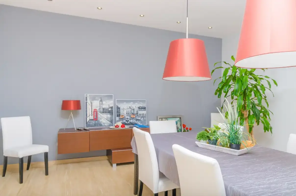 Comedor con mesa, asientos tapizados y lámparas colgantes rojas.