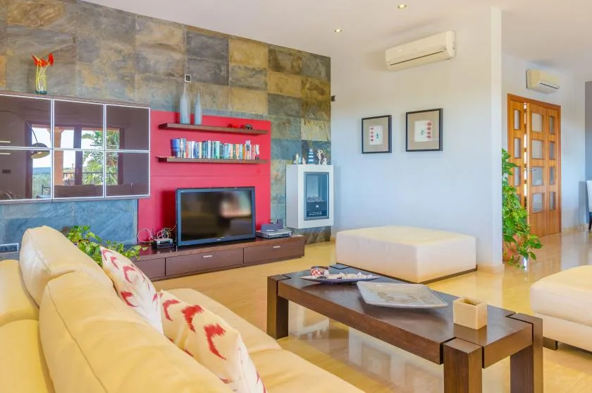 Una sala luminosa con asientos, una mesa de centro y un televisor frente a una pared de aspecto pétreo.