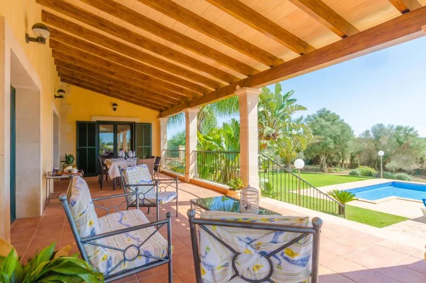 Una terraza exterior cubierta da a un jardín y una piscina.
