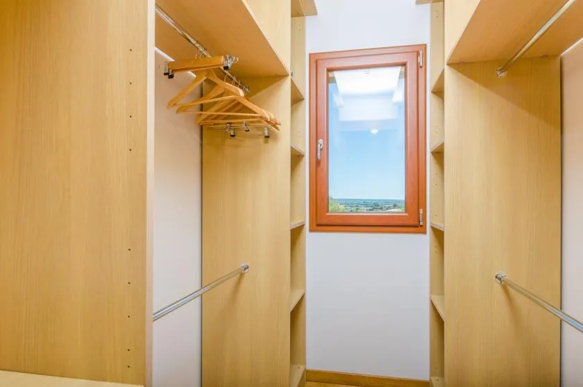 Un vestidor con estantes de madera, barras para colgar ropa y una ventana.
