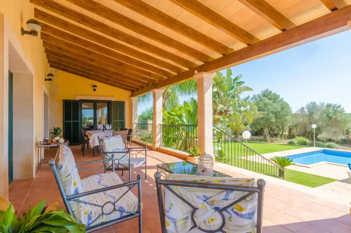 Un patio cubierto con asientos al aire libre da a un césped y una piscina.