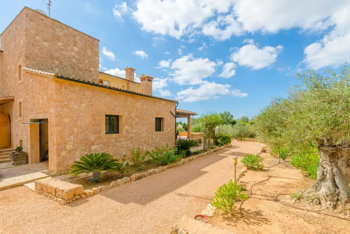 Un edificio de piedra junto a un camino de grava soleado y un jardín.