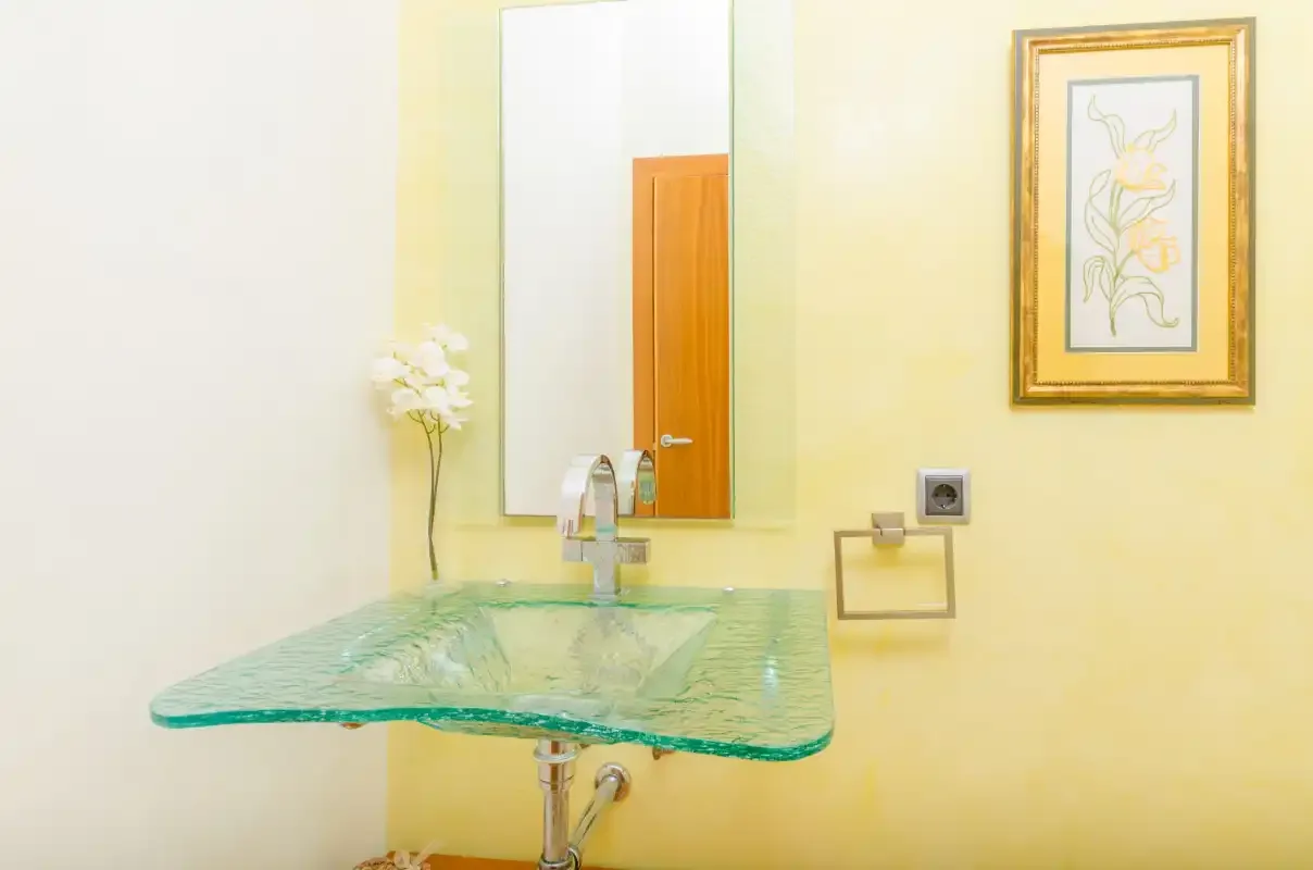 Un lavabo de baño con fregadero de vidrio, espejo y cuadro enmarcado.