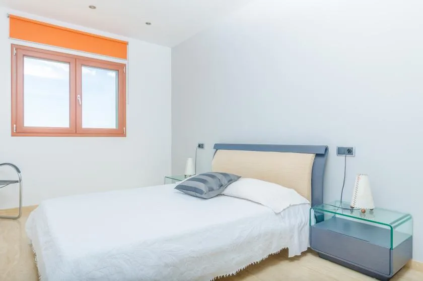 Un dormitorio con una cama junto a una ventana y una mesa de noche de vidrio.