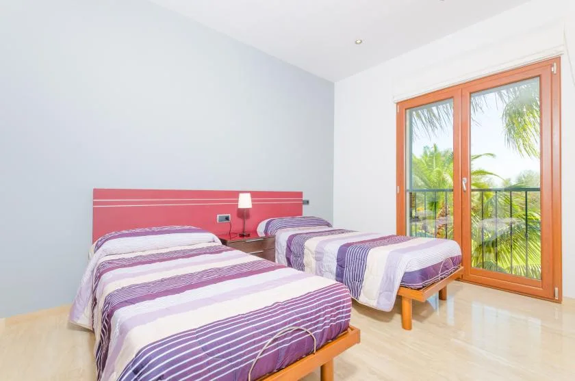 Un dormitorio con dos camas y puertas de vidrio que dan a una vista frondosa.