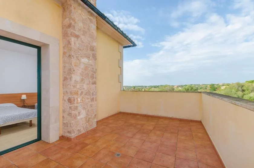 Una terraza exterior con suelo de baldosas junto a un dormitorio, con un muro bajo y cielo abierto.