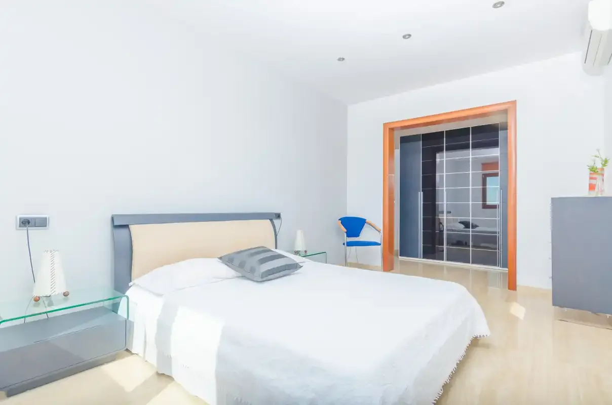 Un dormitorio luminoso con una cama bien tendida y un armario con puertas de cristal.