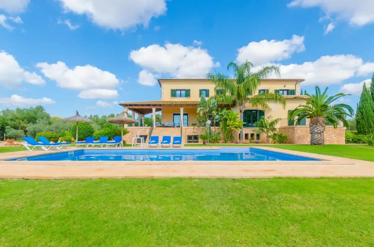 Una casa grande se alza detrás de una piscina y un césped verde.