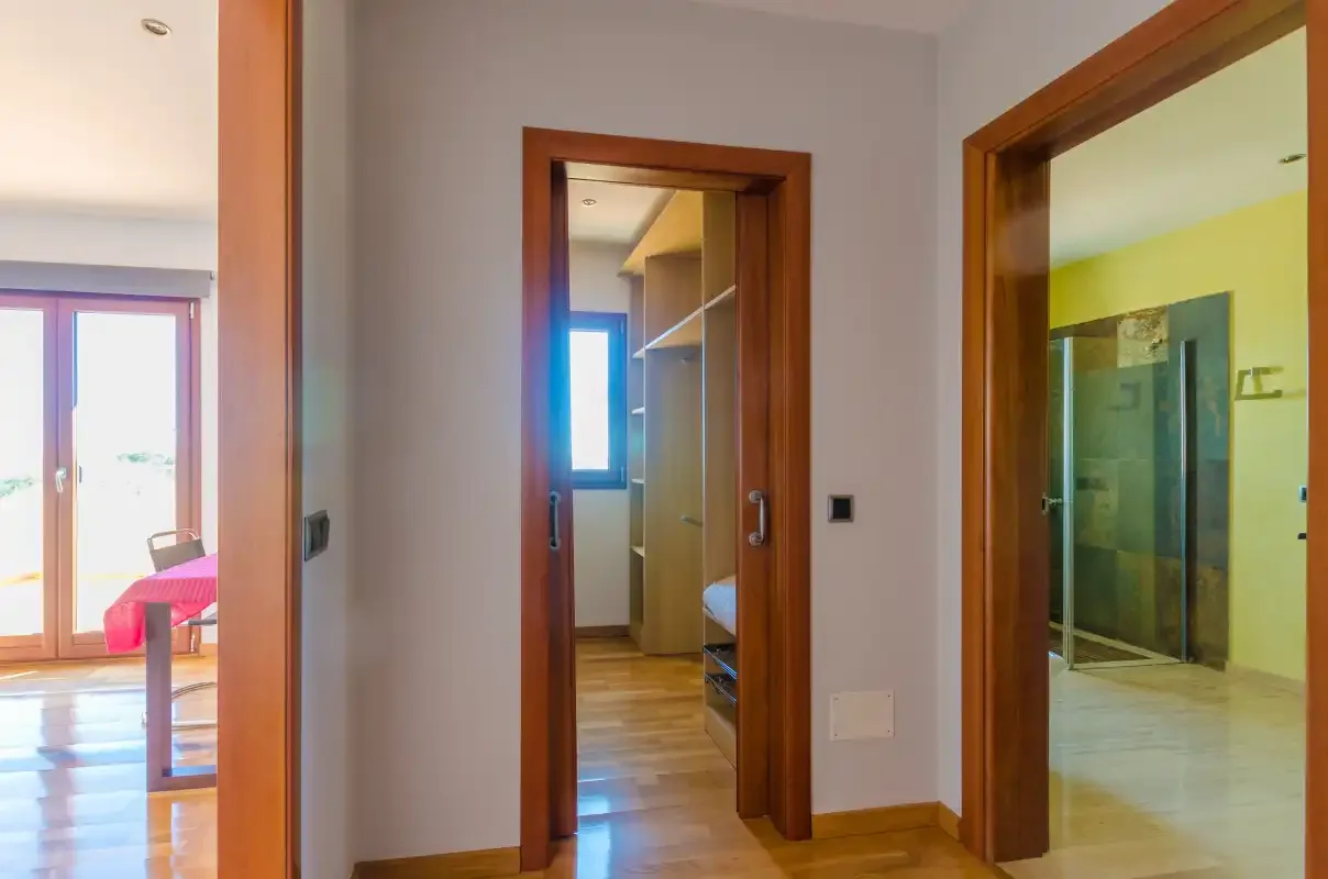 Un pasillo conecta una habitación luminosa, una habitación estrecha y un baño con ducha.