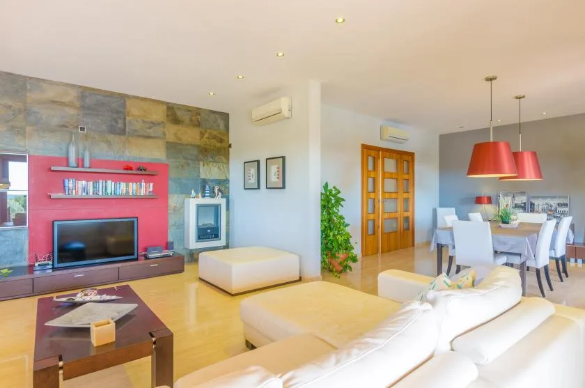 Una luminosa sala de estar y comedor con pared de televisión y mesa de comedor blanca.